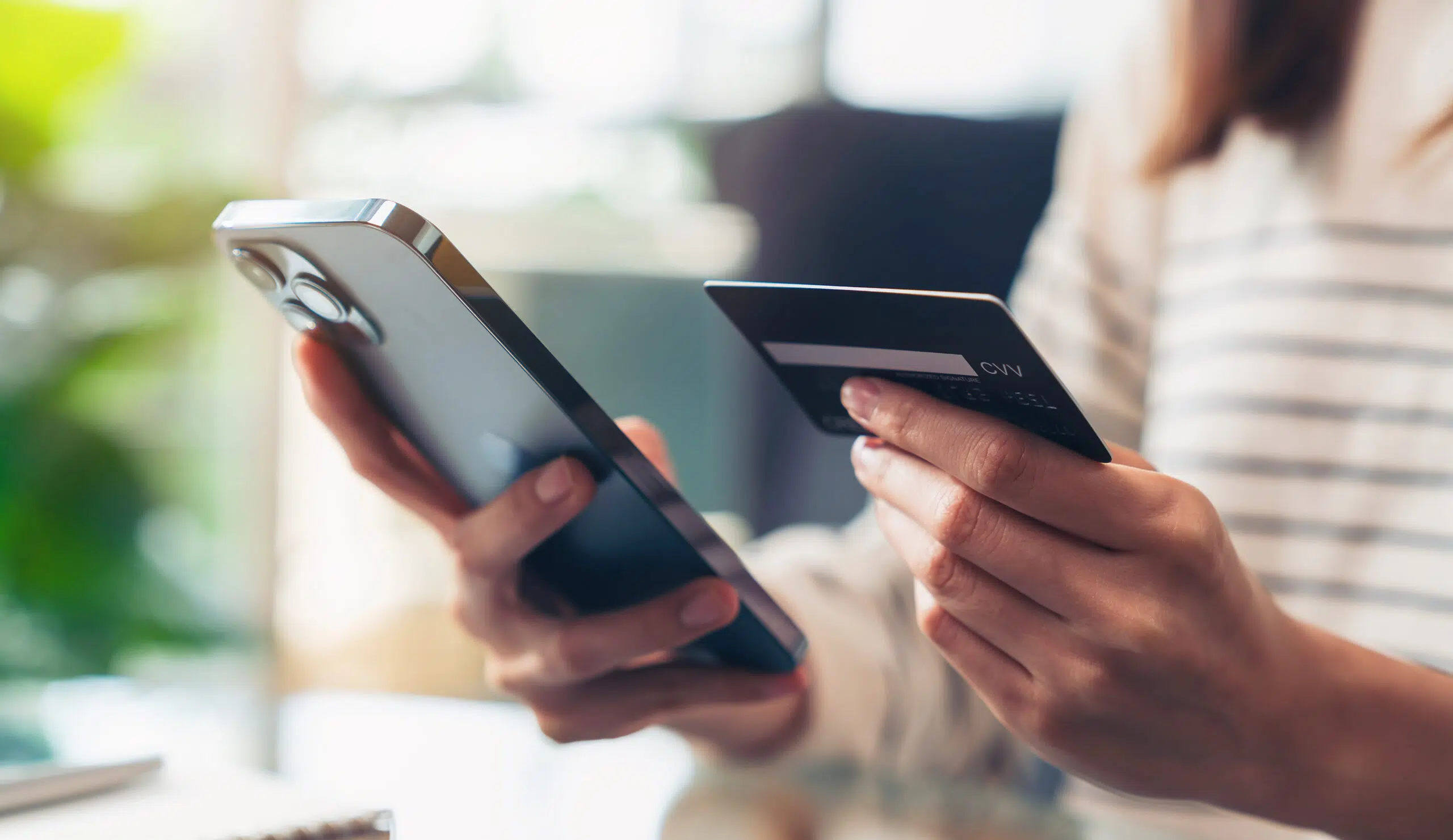 Woman holding a credit card in her left hand and using smartphone in her right hand for shopping online with payment on internet banking.