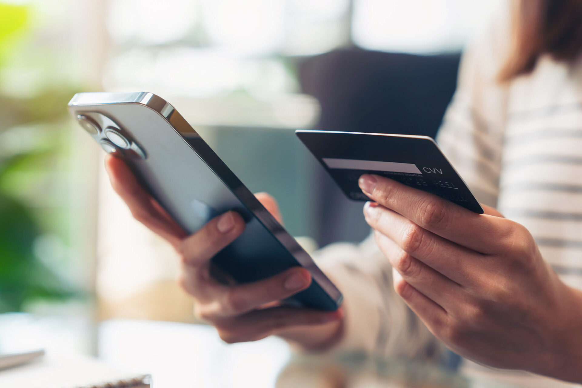 Woman holding a credit card in her left hand and using smartphone in her right hand for shopping online with payment on internet banking.