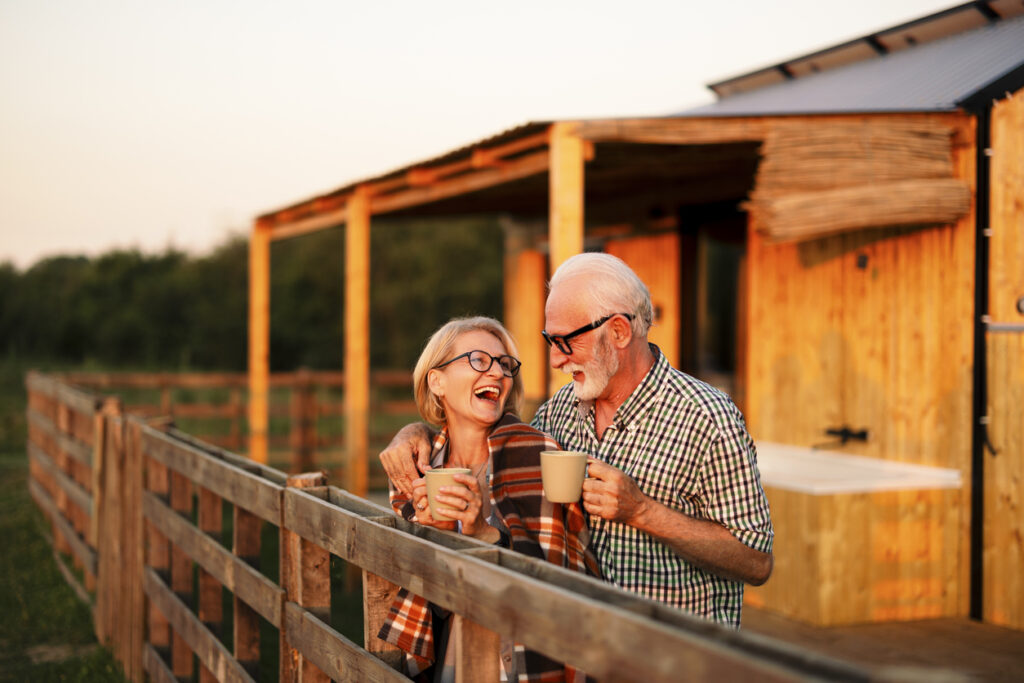 Happy senior couple is on their vacation and spending the evening on the cabin patio, keeping warm with a blanket and a cup of coffee.