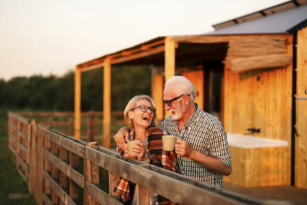 Happy senior couple is on their vacation and spending the evening on the cabin patio, keeping warm with a blanket and a cup of coffee.