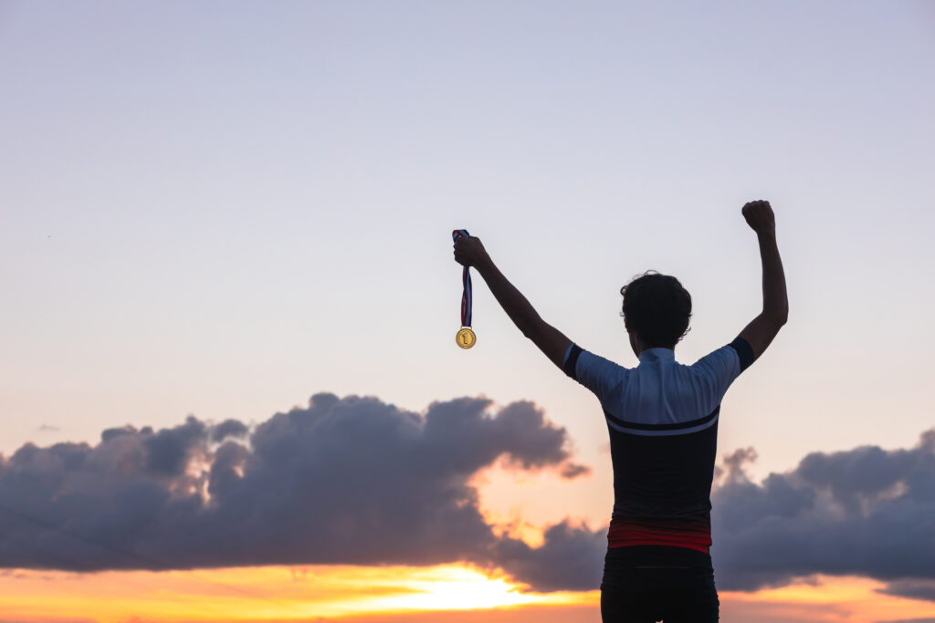 Silhouette of an athlete celebrating the gold medal against a sunset sky adorned with golden clouds in the background. Ideal for conveying the spirit of success in sporting events.